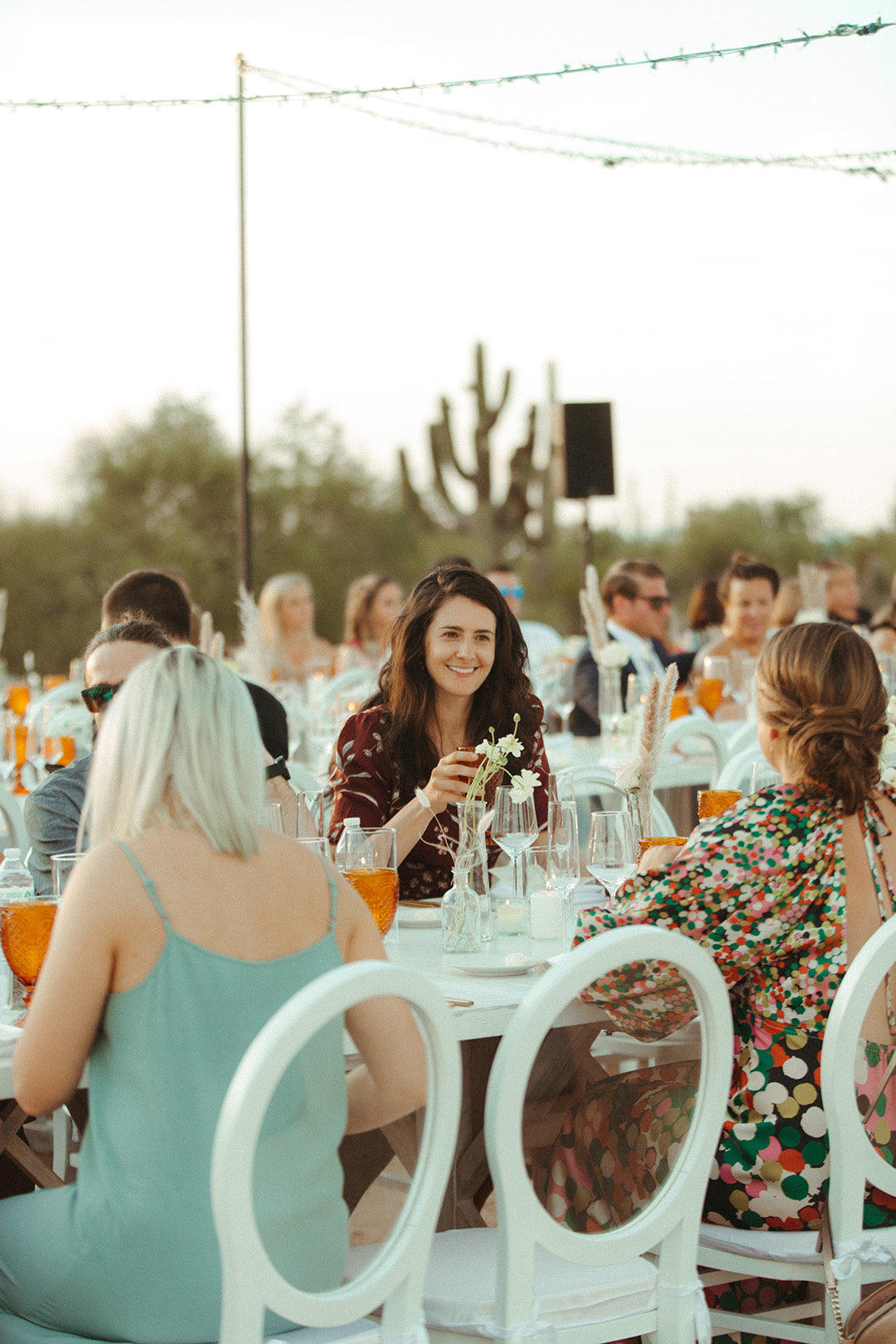 A woman sits at a wedding reception table with bud vases of florals at sunset