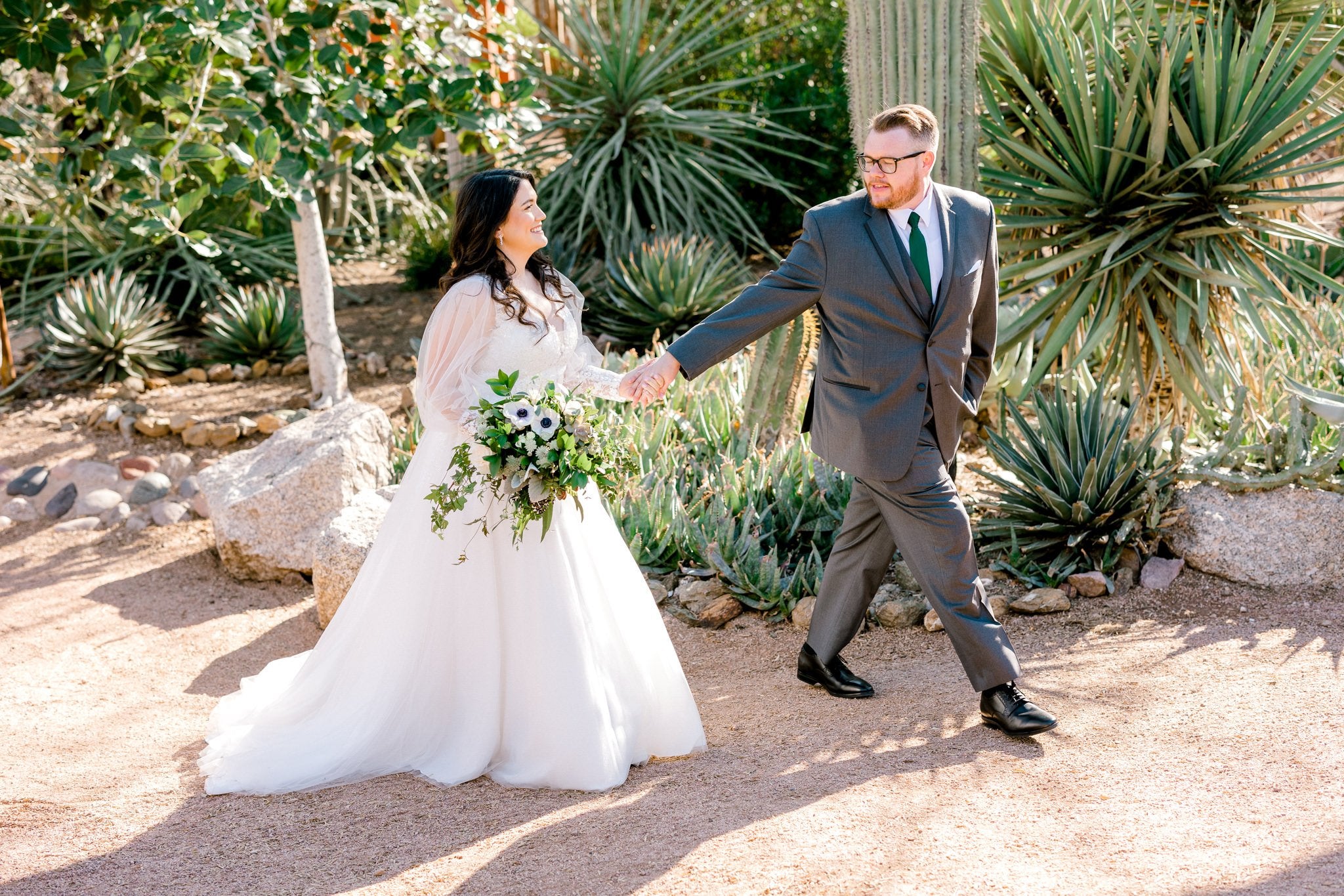 Bride and groom walking through the desert holding large bridal bouquet of flowers and greenery
