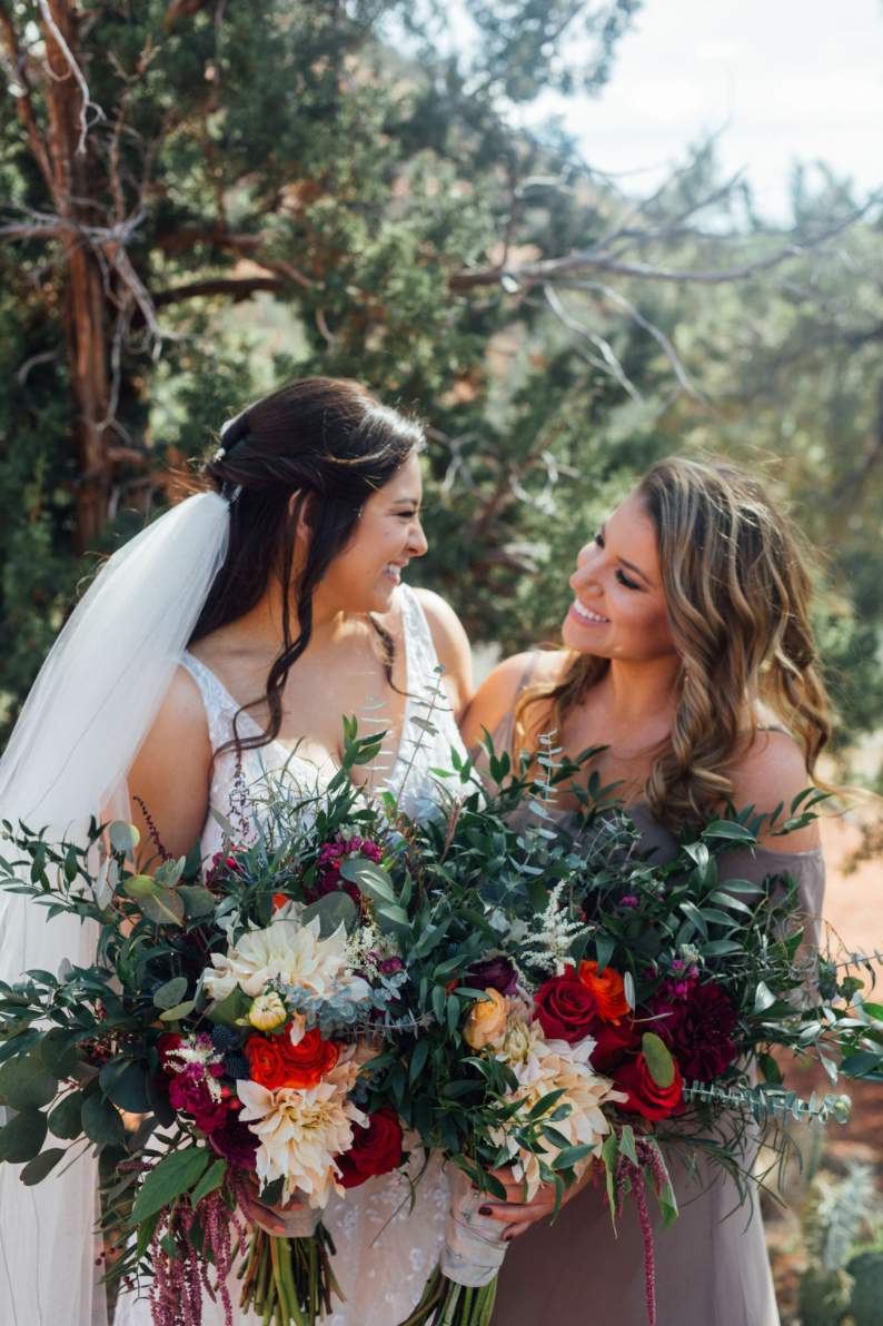 A bride and her bridesmaid holding two large wedding bouquets in front of a desert backdrop in Arizona
