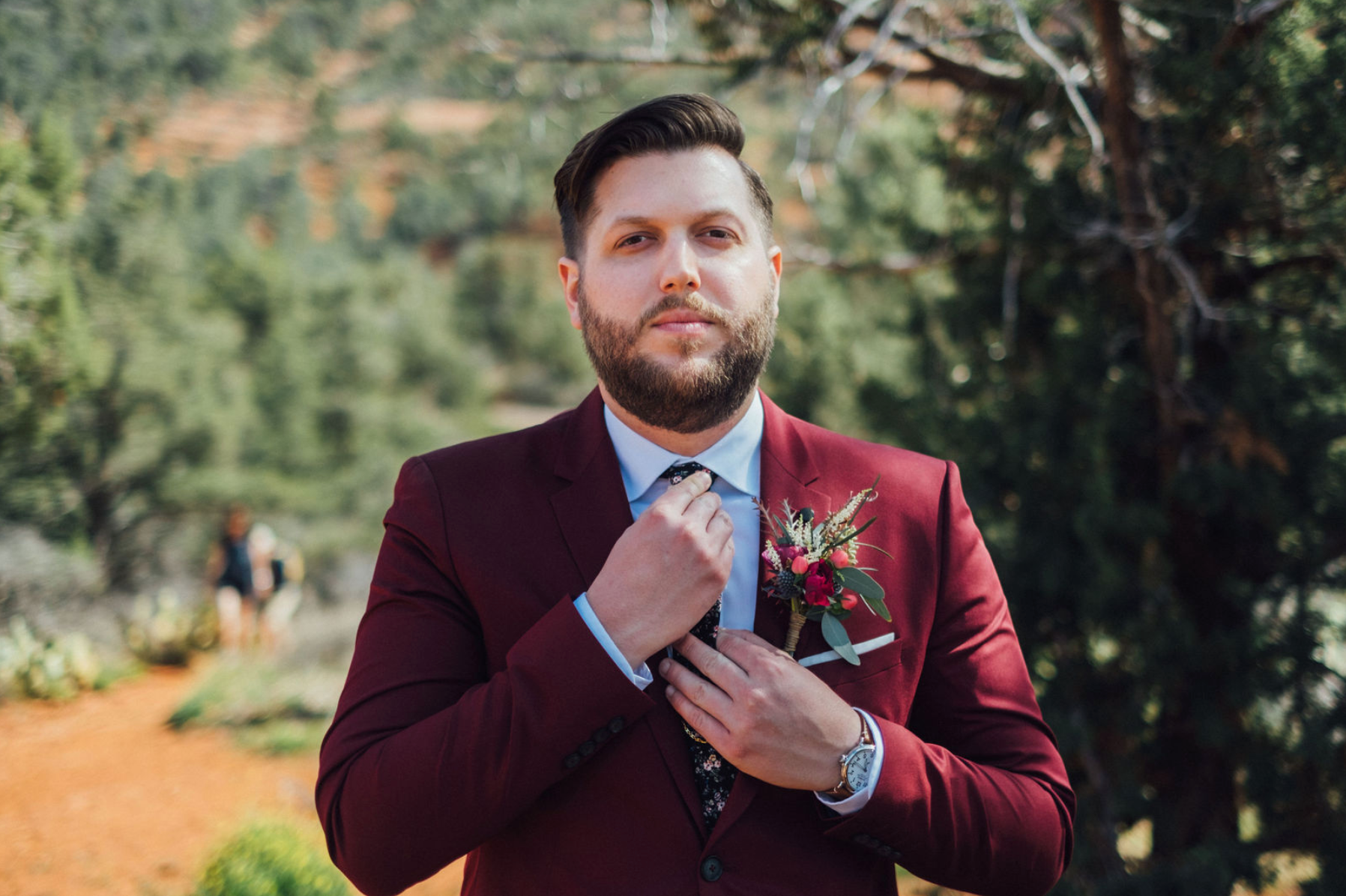 A groom in a burgundy maroon suit with a colorful boutonniere in a desert setting