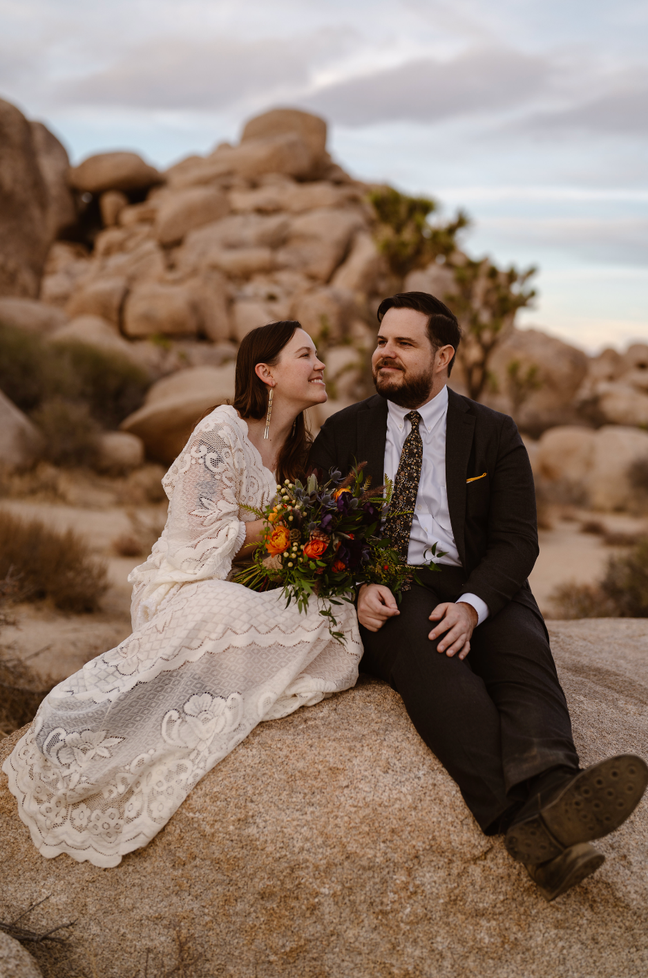 Bride and groom posing on rocks at their desert elopement, holding her bouquet