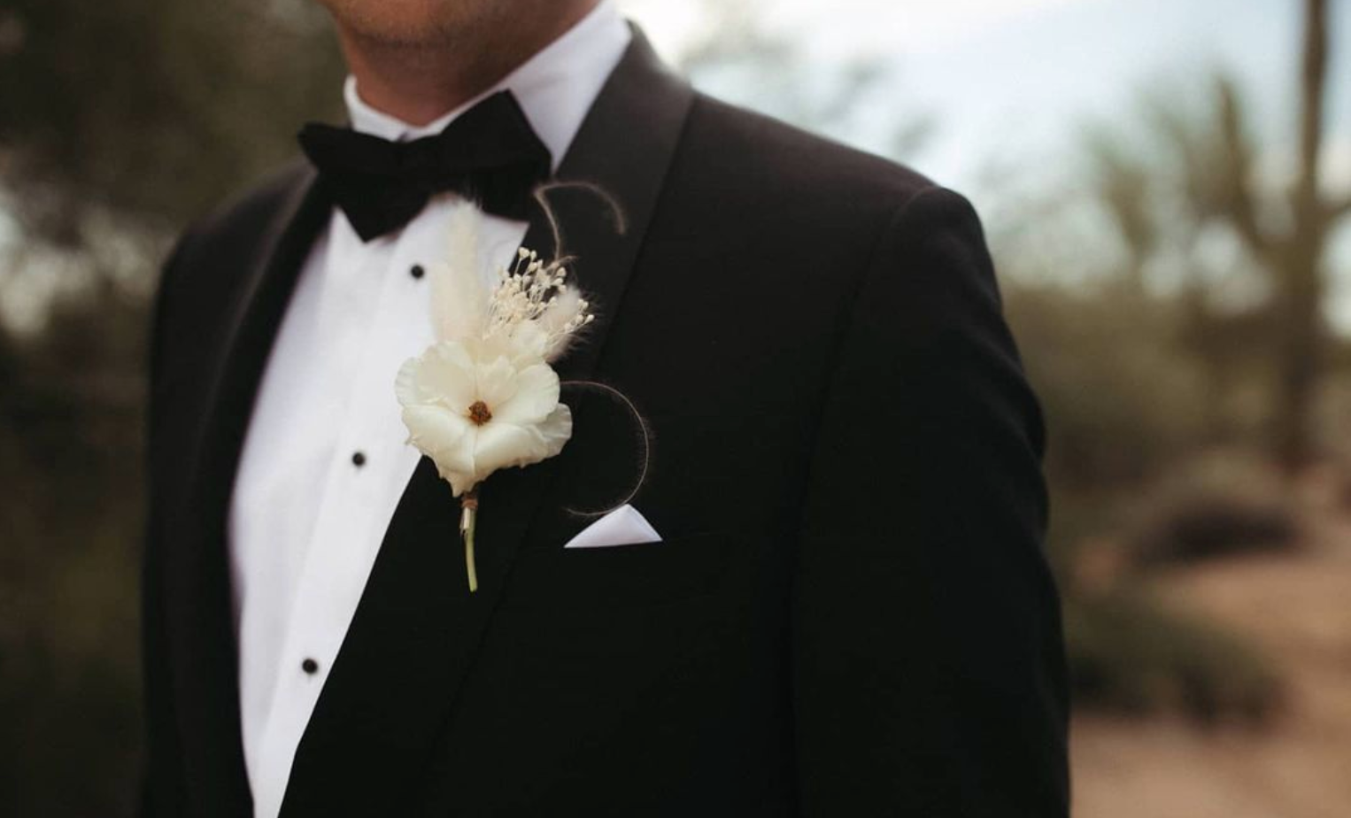 Groom wearing a tuxedo with a boutonniere in a desert wedding setting