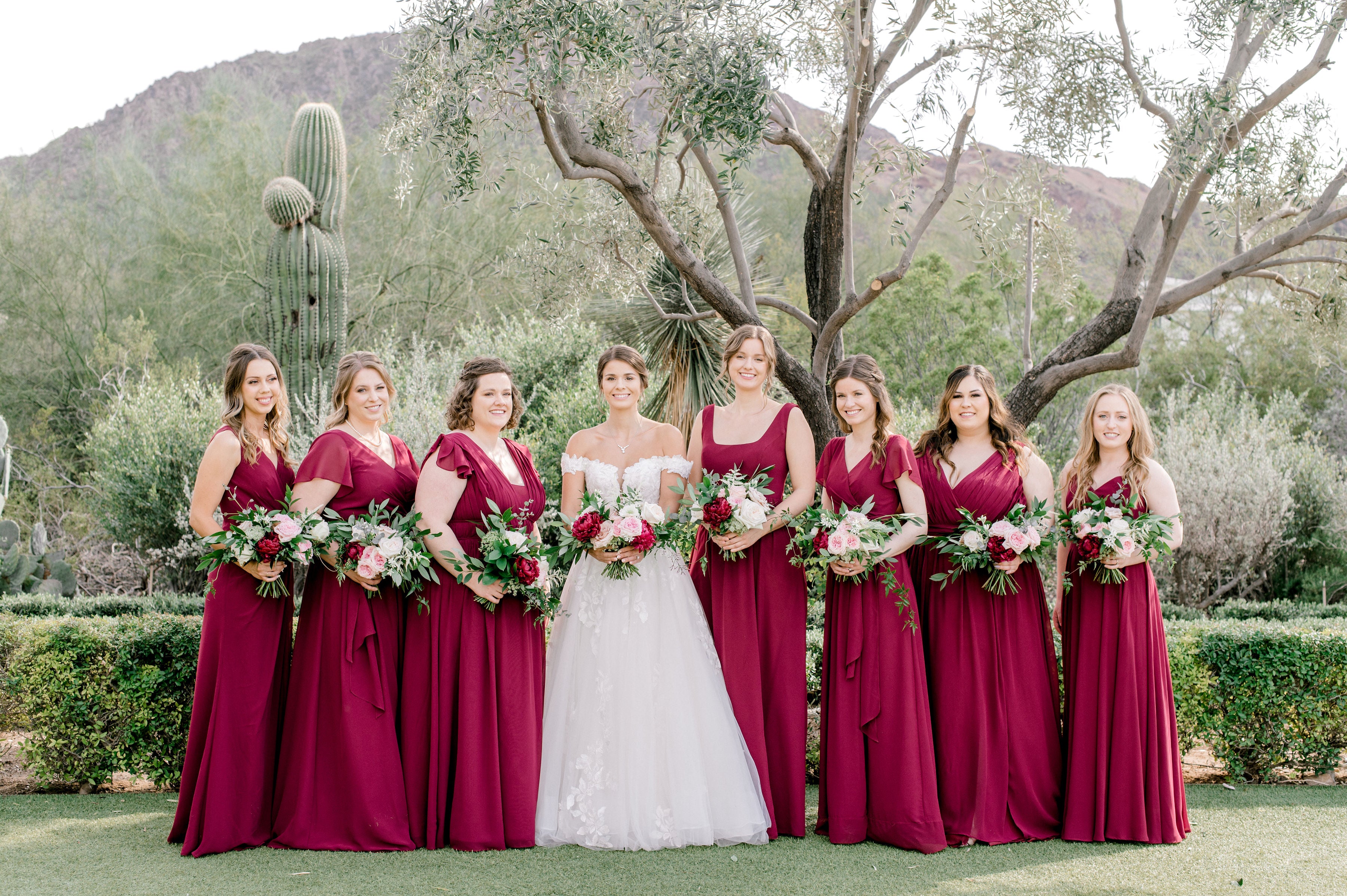 A bride and her bridesmaids pose with their flower bouquets in front of Camelback Moutnain at El Chorro